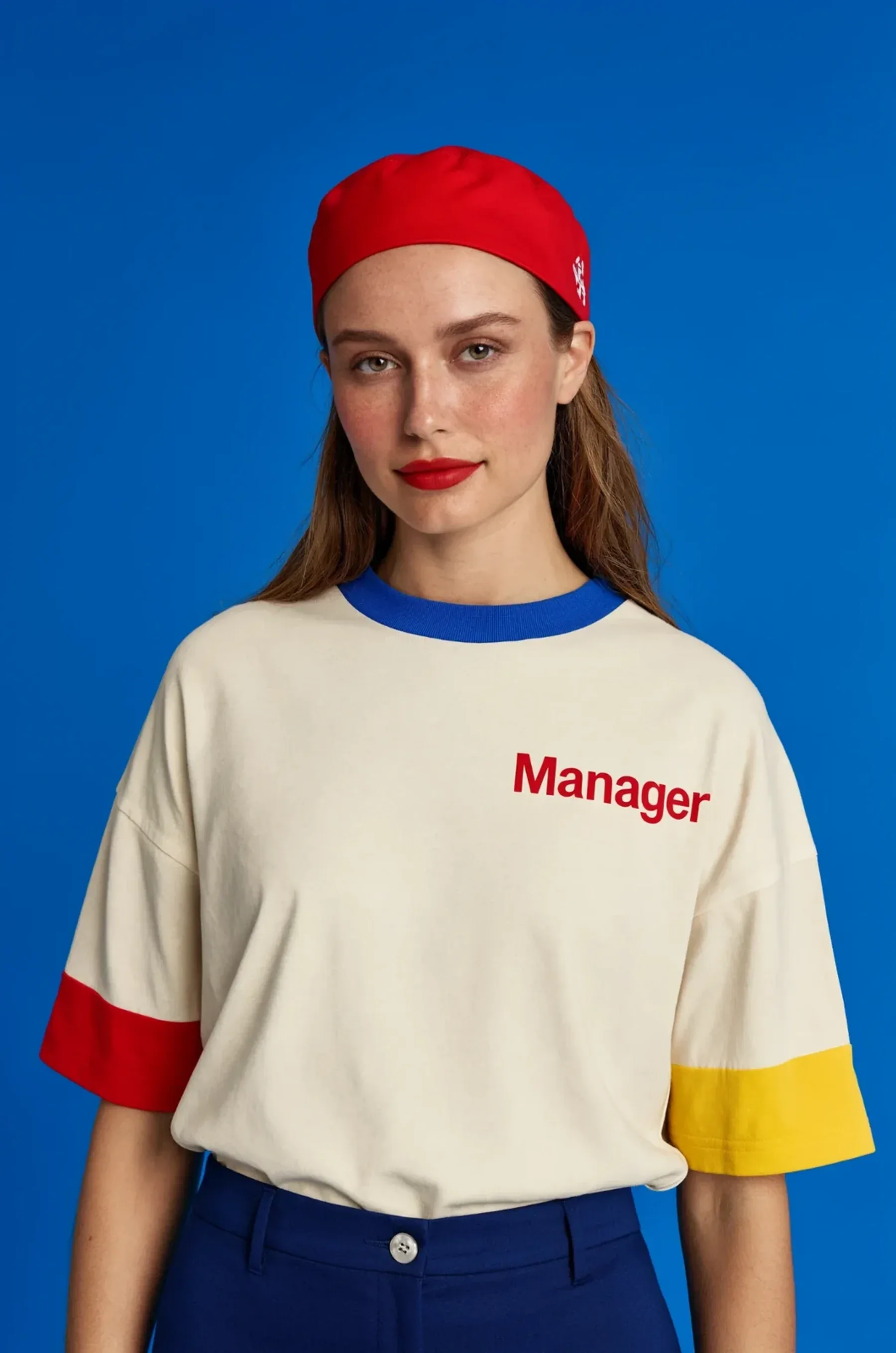 Editorial portrait of a woman in a red cap against a cobalt backdrop